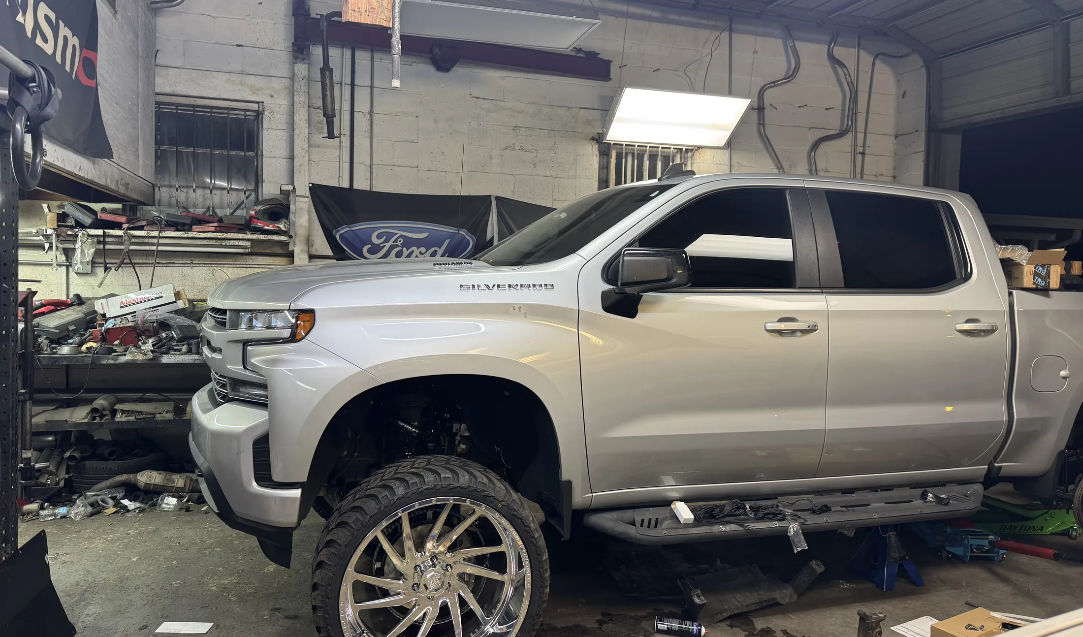 A silver Chevy Silverado crew cab up on the lift inside the shop bay