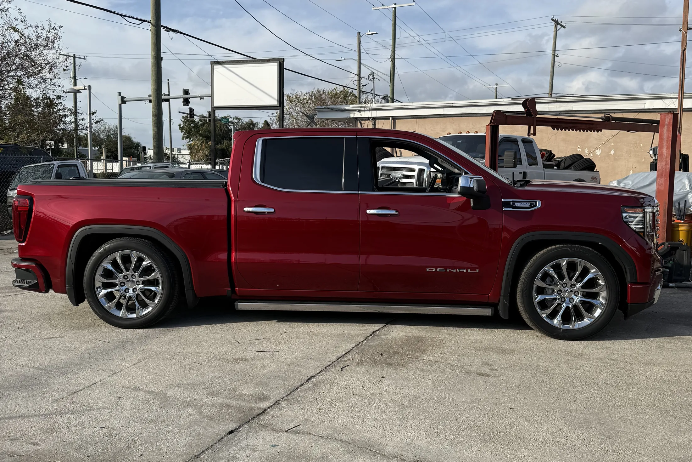 A red GMC Sierra Denali crew cab lowered on polished chrome wheels, parked side on at the shop